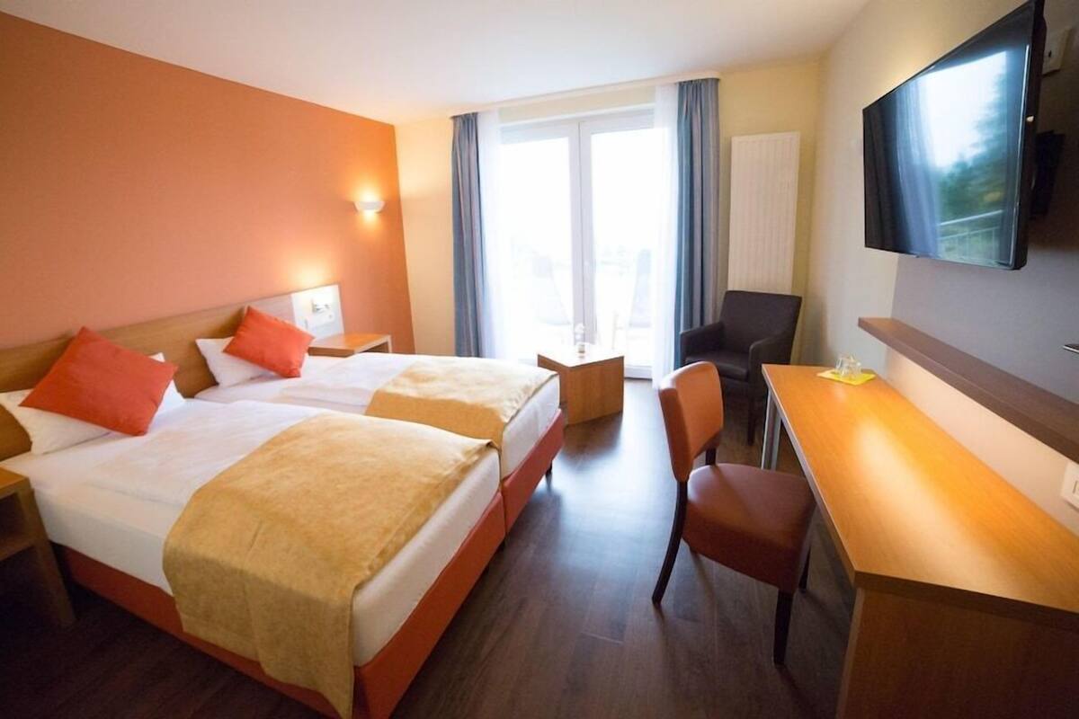 Habitación de hotel con dos camas, un escritorio, una silla, un televisor y una ventana con cortinas.