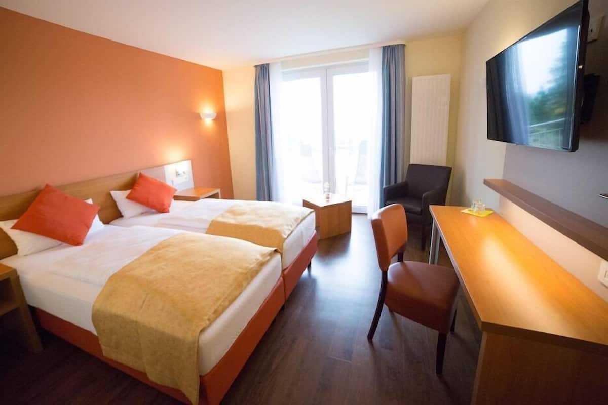 A hotel room with two beds, a desk, a chair, a TV, and a window with curtains.