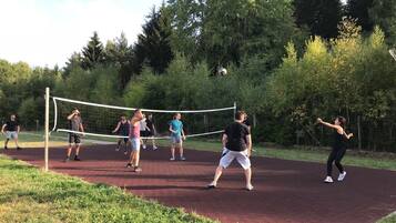 A group of people playing volleyball on an outdoor court surrounded by trees.