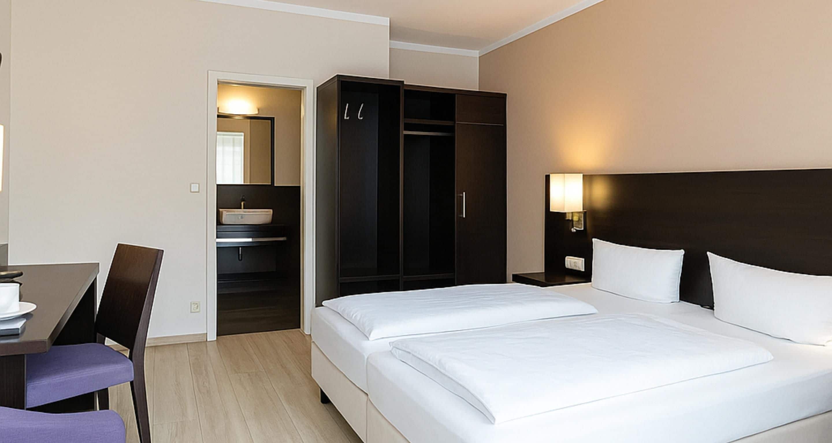 A hotel room with a bed, a desk, a chair, a wardrobe, and a bathroom.