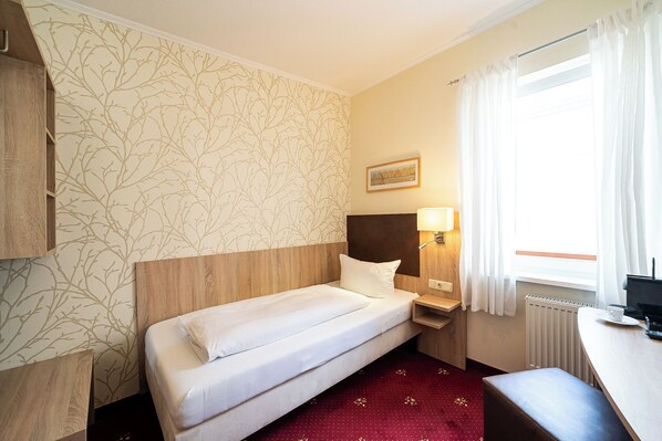 A hotel room with a single bed, a nightstand with a lamp, a window with curtains, and a radiator. - Wilhelmshaven Ahoi, Sure Hotel Collection by Best Western (Wilhelmshaven)