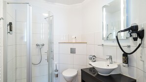 A modern bathroom with a glass shower enclosure, a white toilet, a black sink, and a hairdryer mounted on the wall. - Wilhelmshaven Ahoi, Sure Hotel Collection by Best Western (Wilhelmshaven)