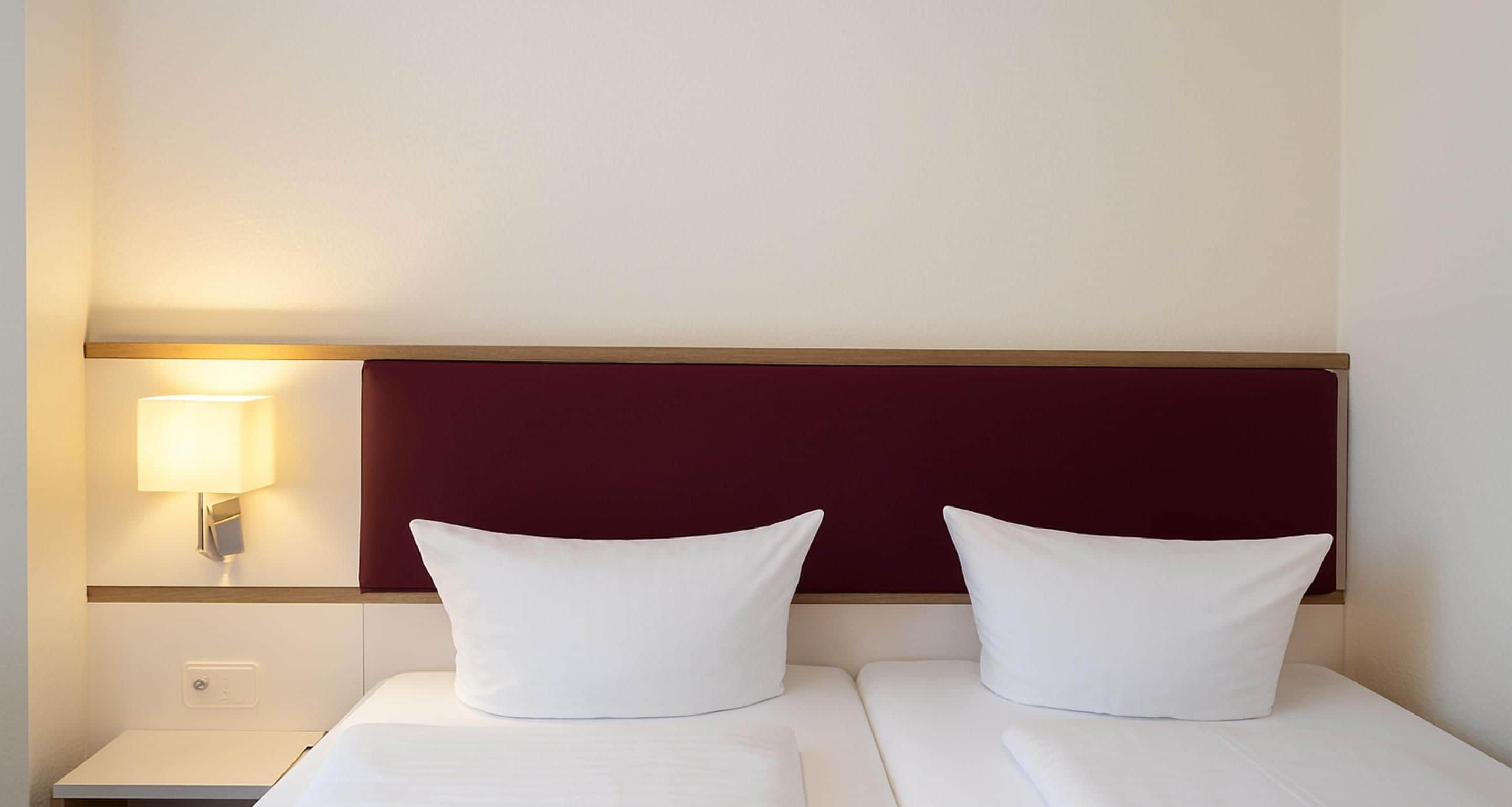 Ein Hotelzimmer mit einem Bett, zwei Kissen, einem Nachttisch und einer Wandleuchte.