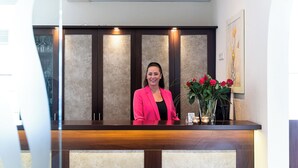 A reception desk with a woman standing behind it, a vase with red roses, and a framed picture on the wall. - Wilhelmshaven Ahoi, Sure Hotel Collection by Best Western (Wilhelmshaven)