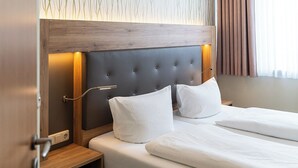 A hotel room with a tufted headboard, two white pillows, a wooden nightstand, and a bed with white bedding. - Wilhelmshaven Ahoi, Sure Hotel Collection by Best Western (Wilhelmshaven)