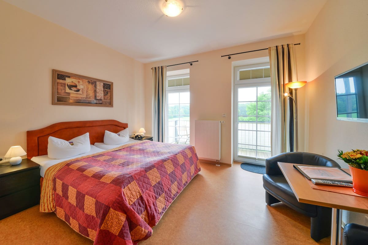 A hotel room with a bed, bedside table, lamp, chair, and a view of the outdoors.
