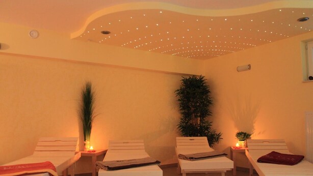 Um salão de spa com duas mesas de massagem, teto com pequenas luzes e um vaso de planta.