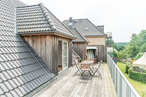 A wooden deck with a table and chairs, a sliding door, and a view of a neighboring house with a tiled roof. - Ostseehotel Rike (Zierow)