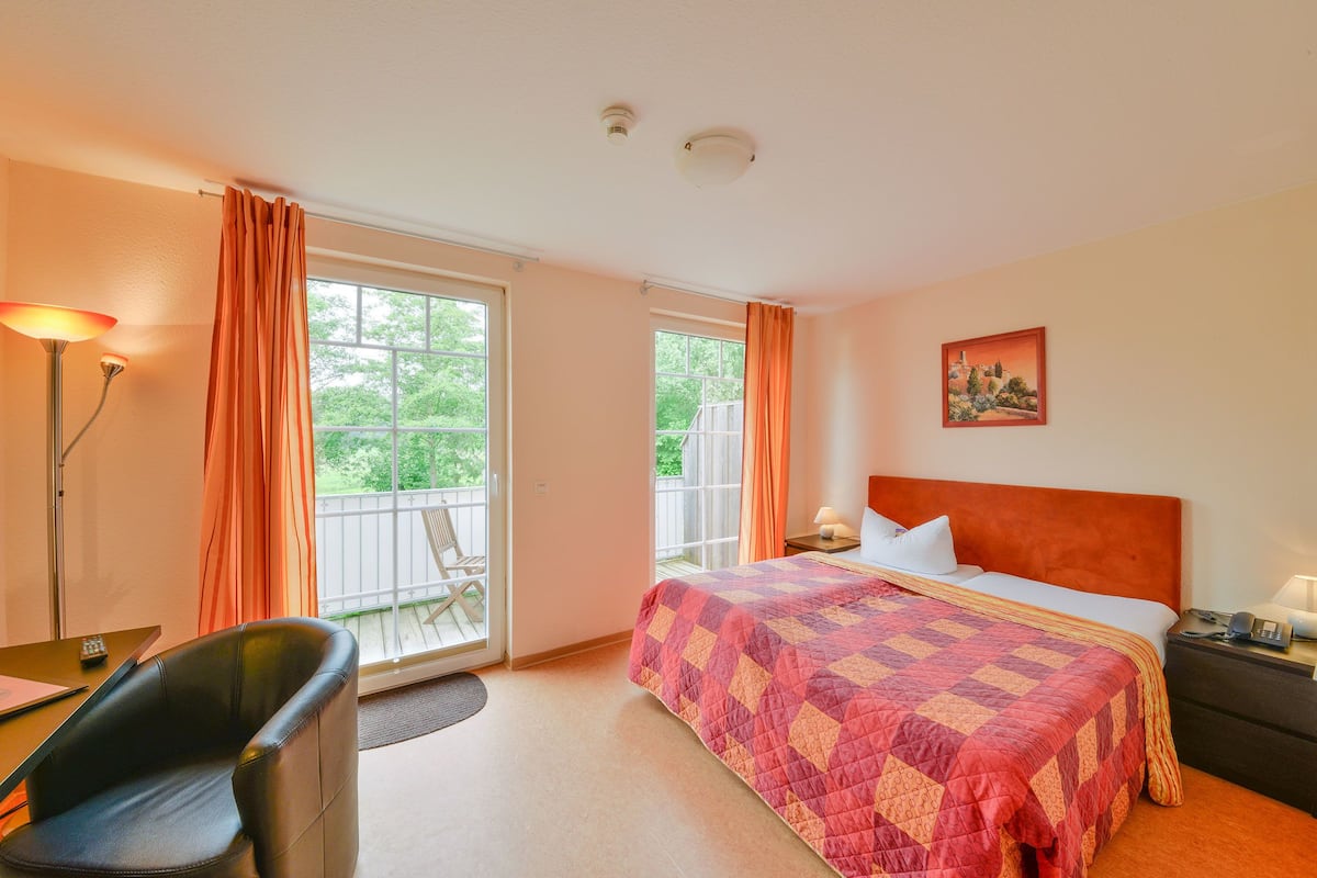 A hotel room with a bed, a desk, a chair, and a balcony with curtains.
