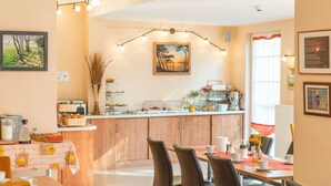 Uma sala de jantar com mesa posta para quatro pessoas, bancada da cozinha com diversos objetos e obras de arte nas paredes.