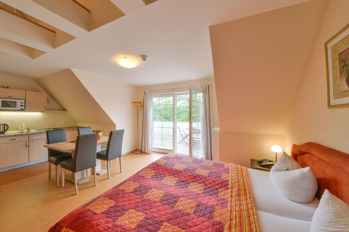 A bedroom with a large bed, a desk, and a kitchenette.