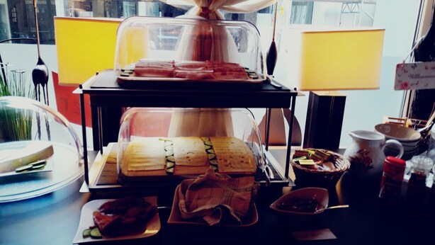 Mostrador de comidas con sándwiches, salsas y aderezos, una máquina de café y vista al exterior.