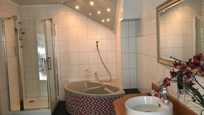 Un baño moderno con ducha de vidrio, una bañera independiente con diseño de mosaico y un lavabo con espejo.