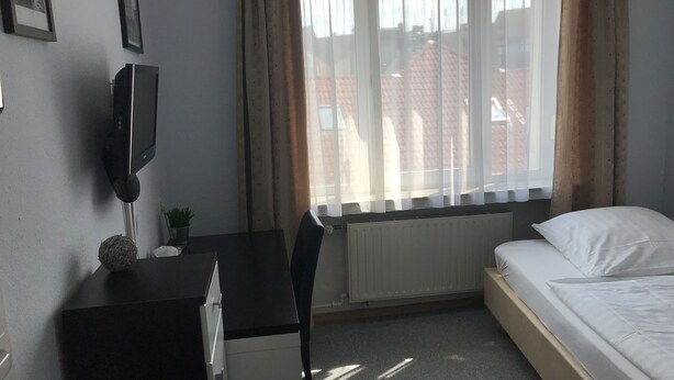 Una camera d'albergo con un letto, una scrivania con una sedia, un termosifone e una finestra con tende.