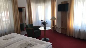 Habitación de hotel con dos camas, un sillón verde, una mesita de noche con una lámpara y un televisor montado en la pared.