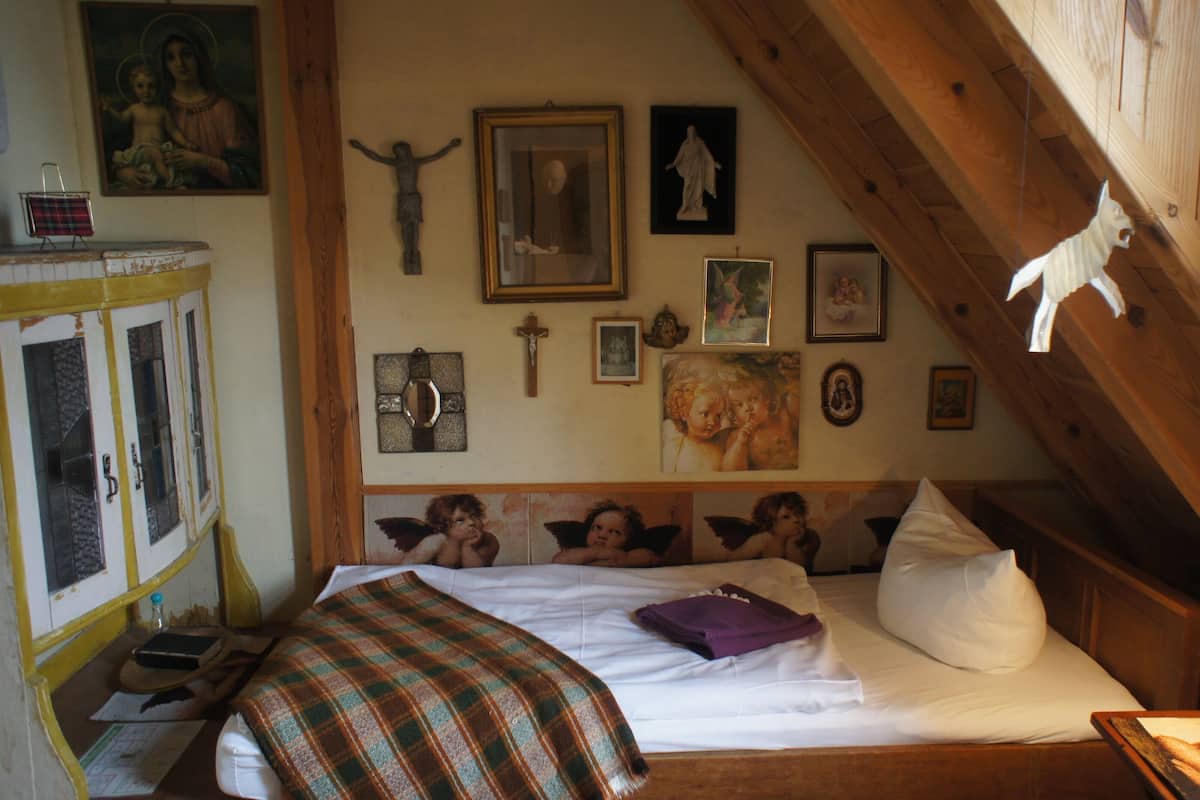 Un dormitorio con cama, vigas de madera y varias obras de arte religiosas en las paredes.