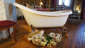 A vintage bathroom with a freestanding bathtub, wooden flooring, and a tray of toiletries.