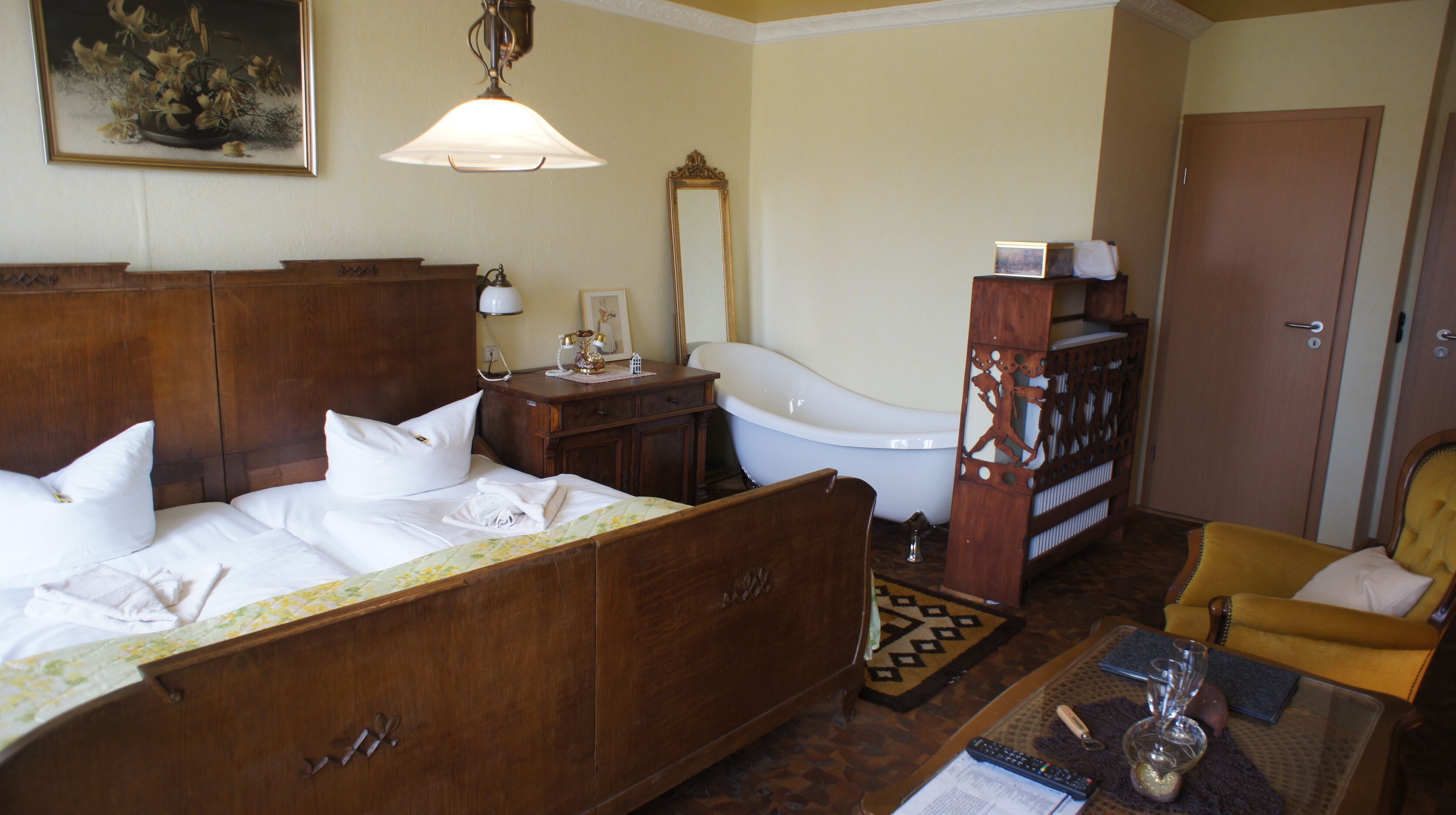 Habitación de hotel con cama de madera, baño blanco, armario de madera y sillón amarillo.