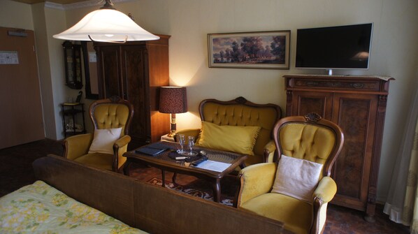 Una habitación de hotel con una cama, dos sillones amarillos, una mesita de madera, una lámpara, un cuadro y un televisor.