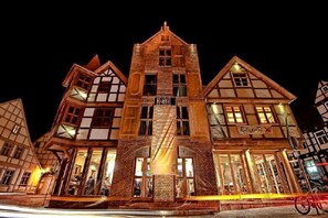 A traditional European-style building with a central tower and two wings, featuring large windows and a sign indicating a restaurant.