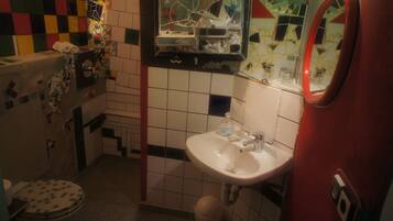 A bathroom with a white sink, a mirror, and a toilet. The walls are tiled with a mix of white and colored tiles.