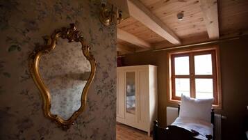 Una habitación con vigas de madera, una cama, un ventanal y un espejo con papel tapiz floral.
