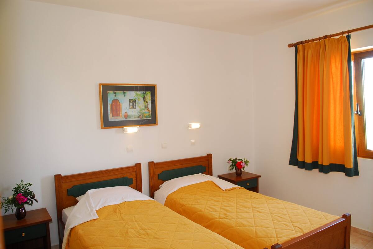 A room with two beds, a painting on the wall, and a window with curtains.
