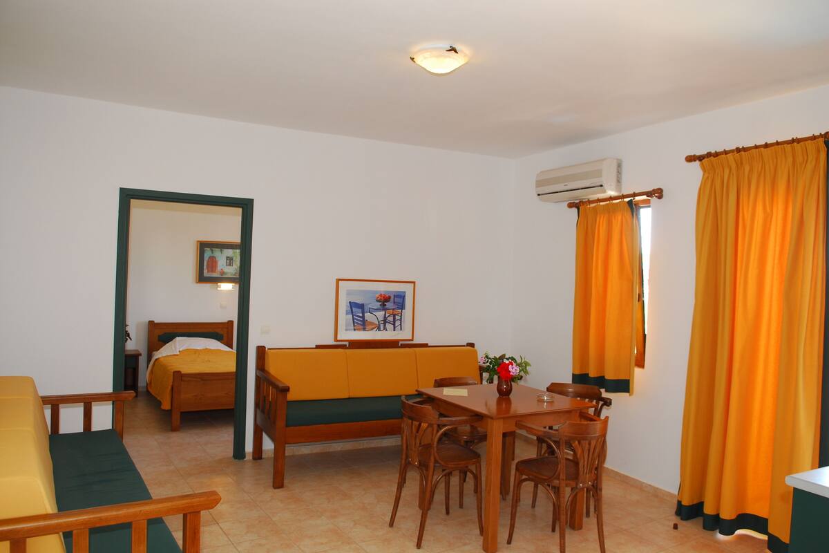 A room with a bed, a sofa, a dining table with chairs, and an air conditioning unit.