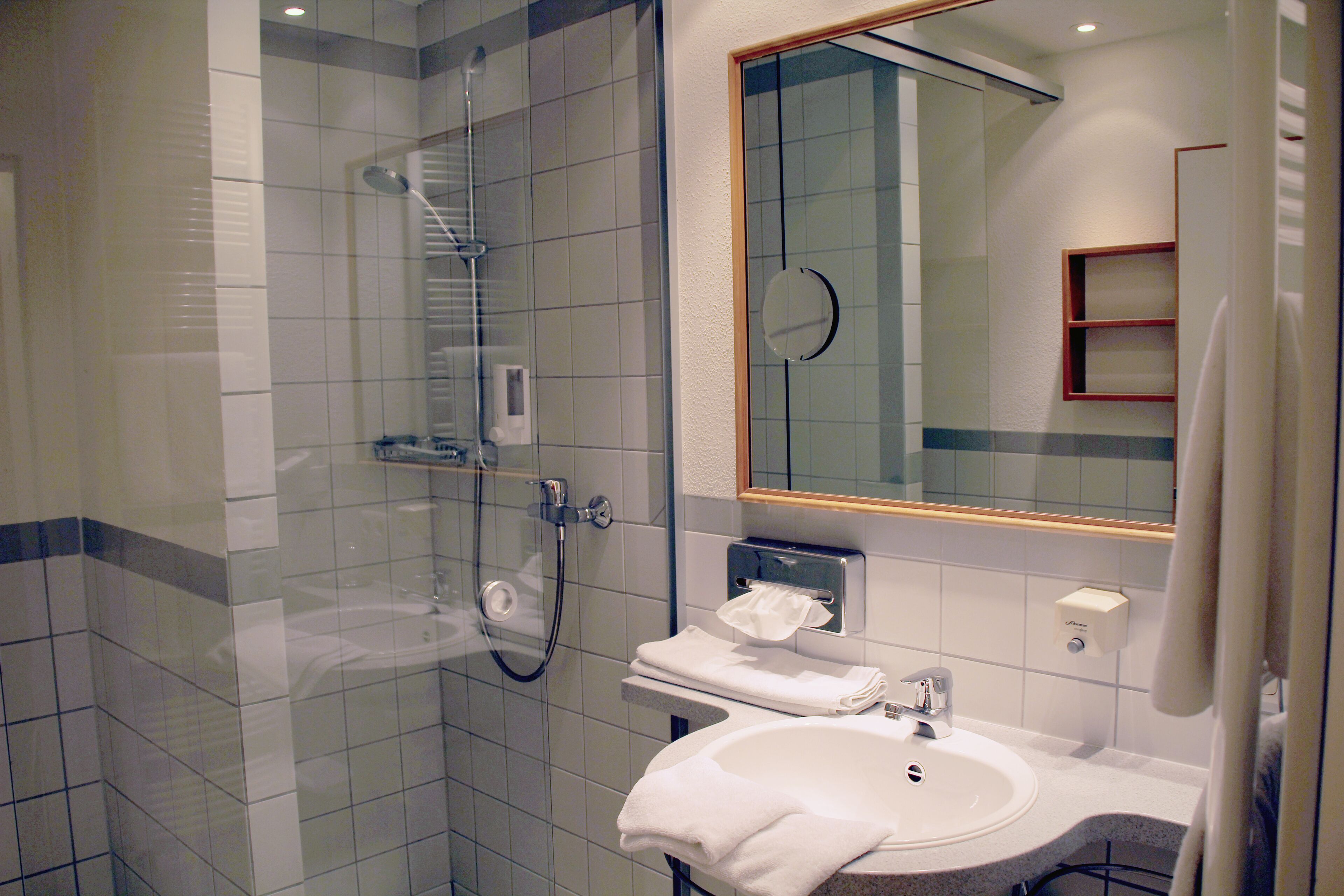 Un baño moderno con ducha de vidrio, un lavabo con espejo y un perchero para toallas.