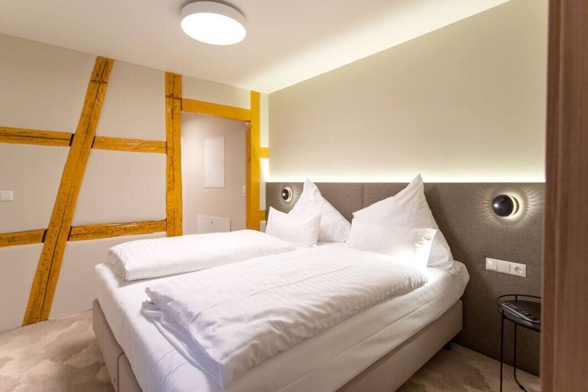 A hotel room with a large bed, a bedside table, and a modern light fixture.