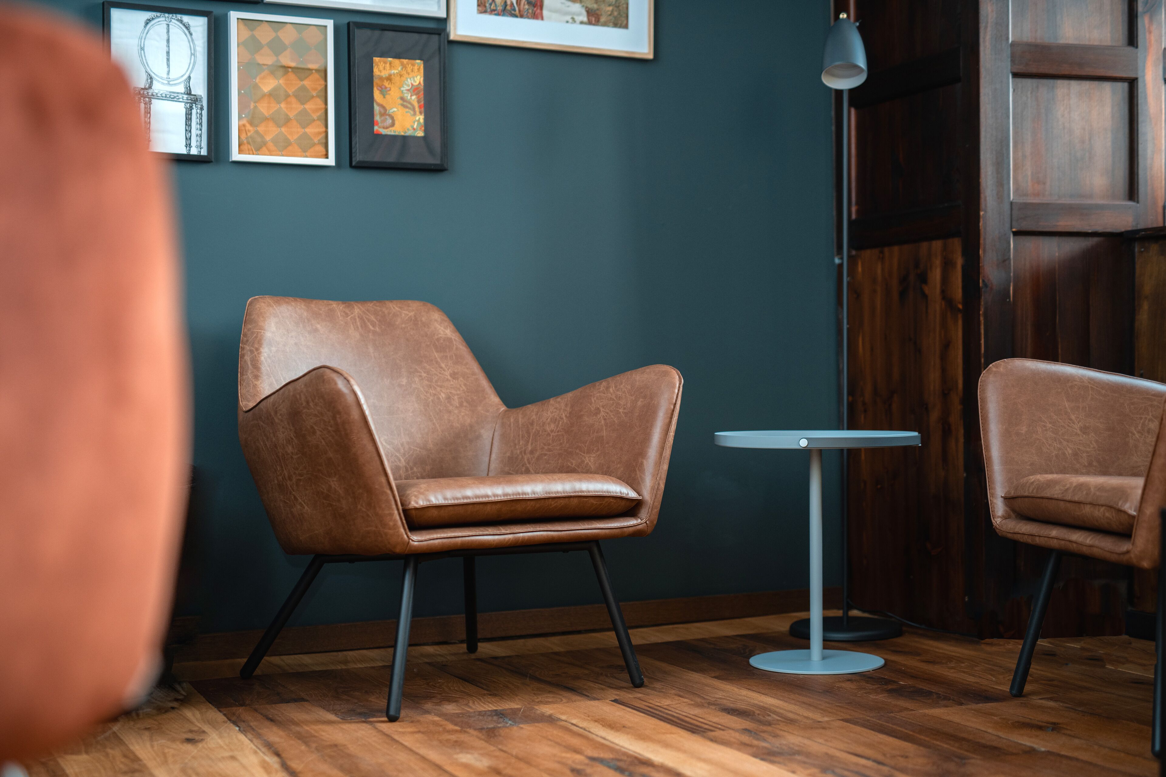 A room with two brown leather chairs, a small round table, and framed artwork on the wall.