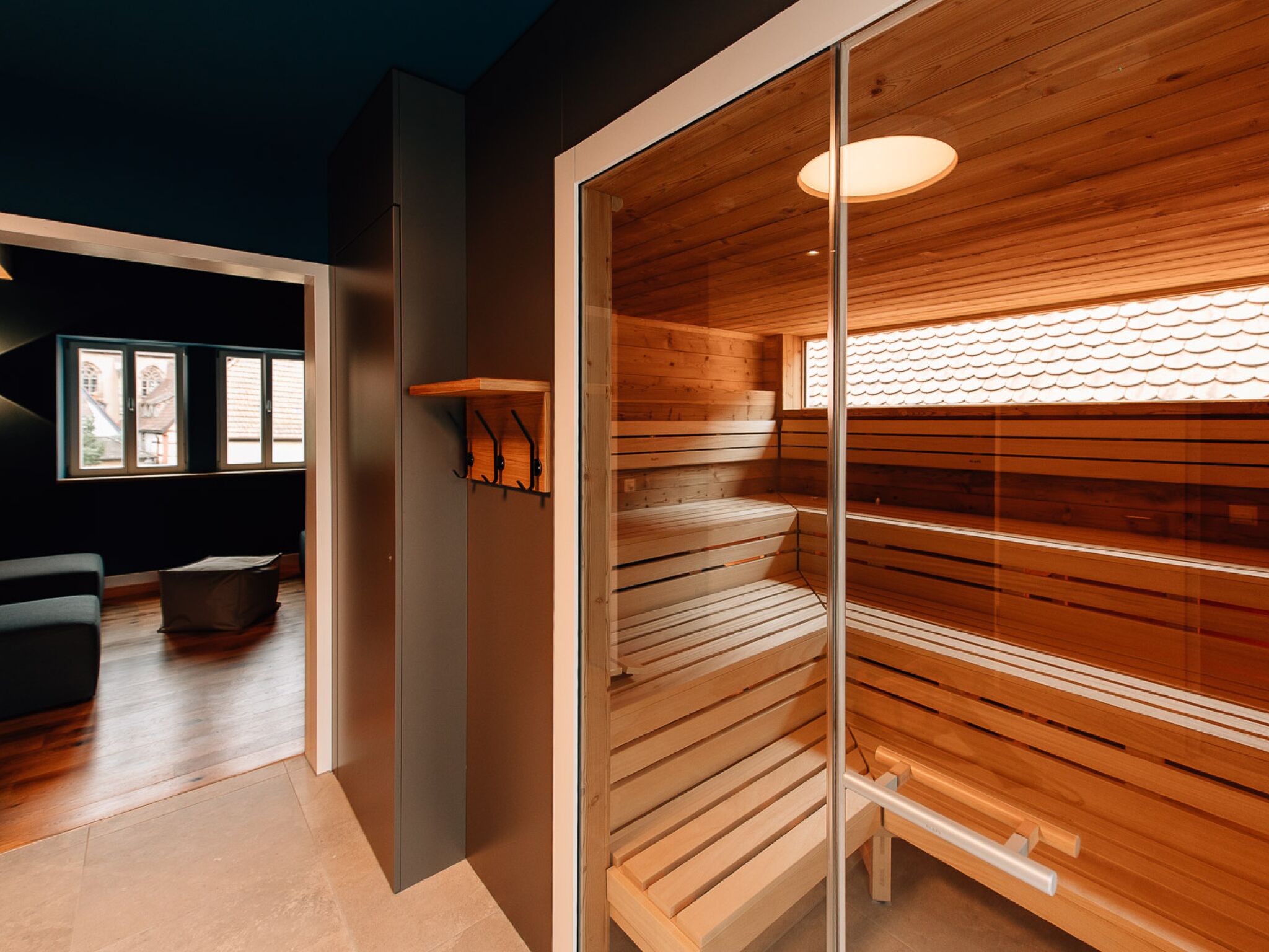 A modern interior with a wooden sauna, a glass partition, and a seating area with a view of the outside.