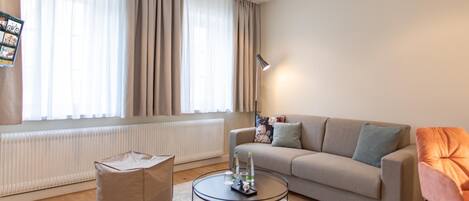 A living room with a sofa, a round coffee table, a chair, a radiator, and a window with curtains.