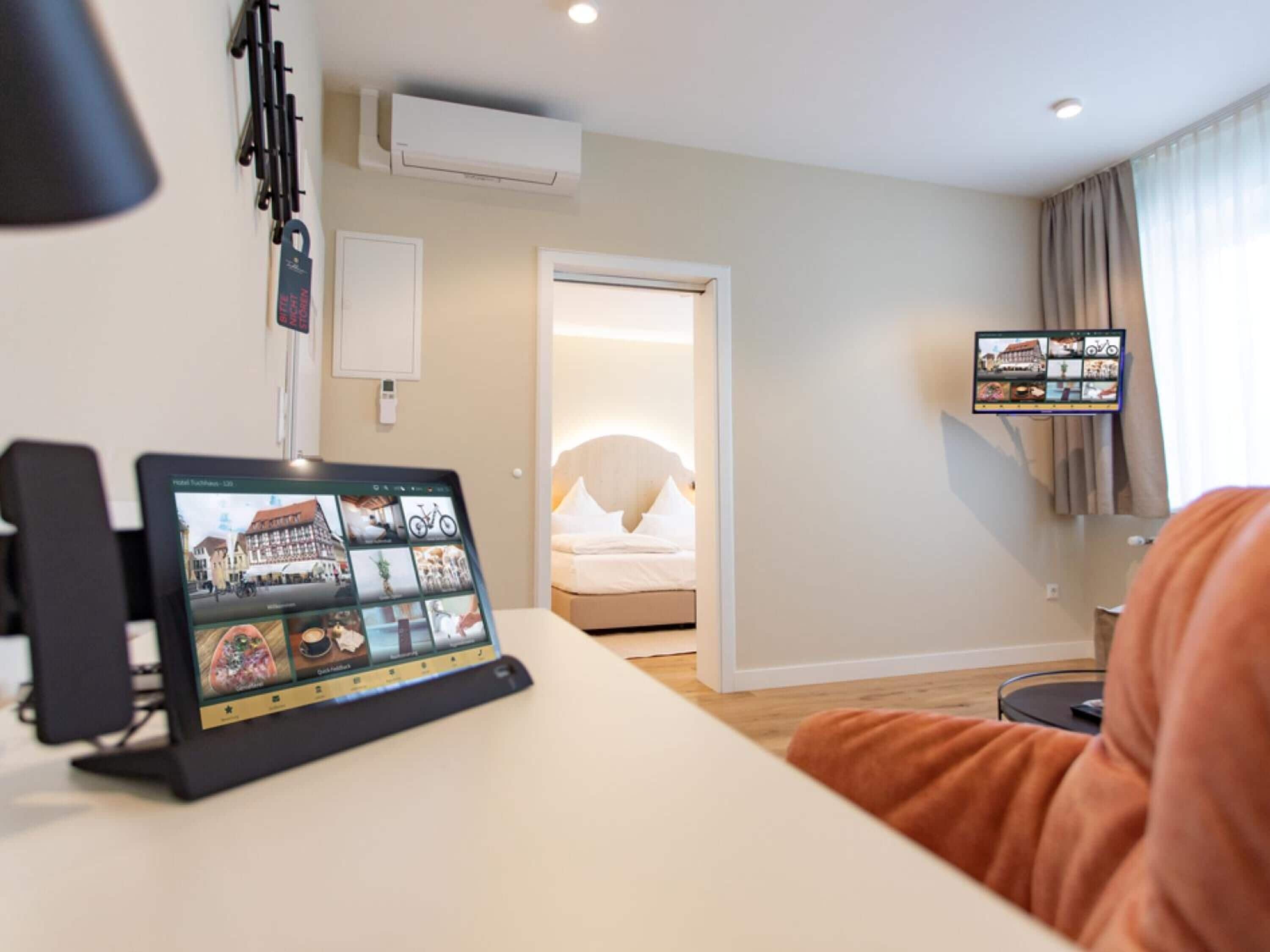 A hotel room with a bed, a TV mounted on the wall, and a tablet displaying a hotel directory.