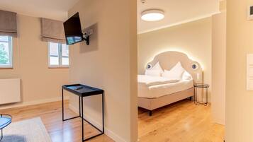 A modern bedroom with a bed, a flat-screen TV mounted on the wall, a small table, and a window with blinds.