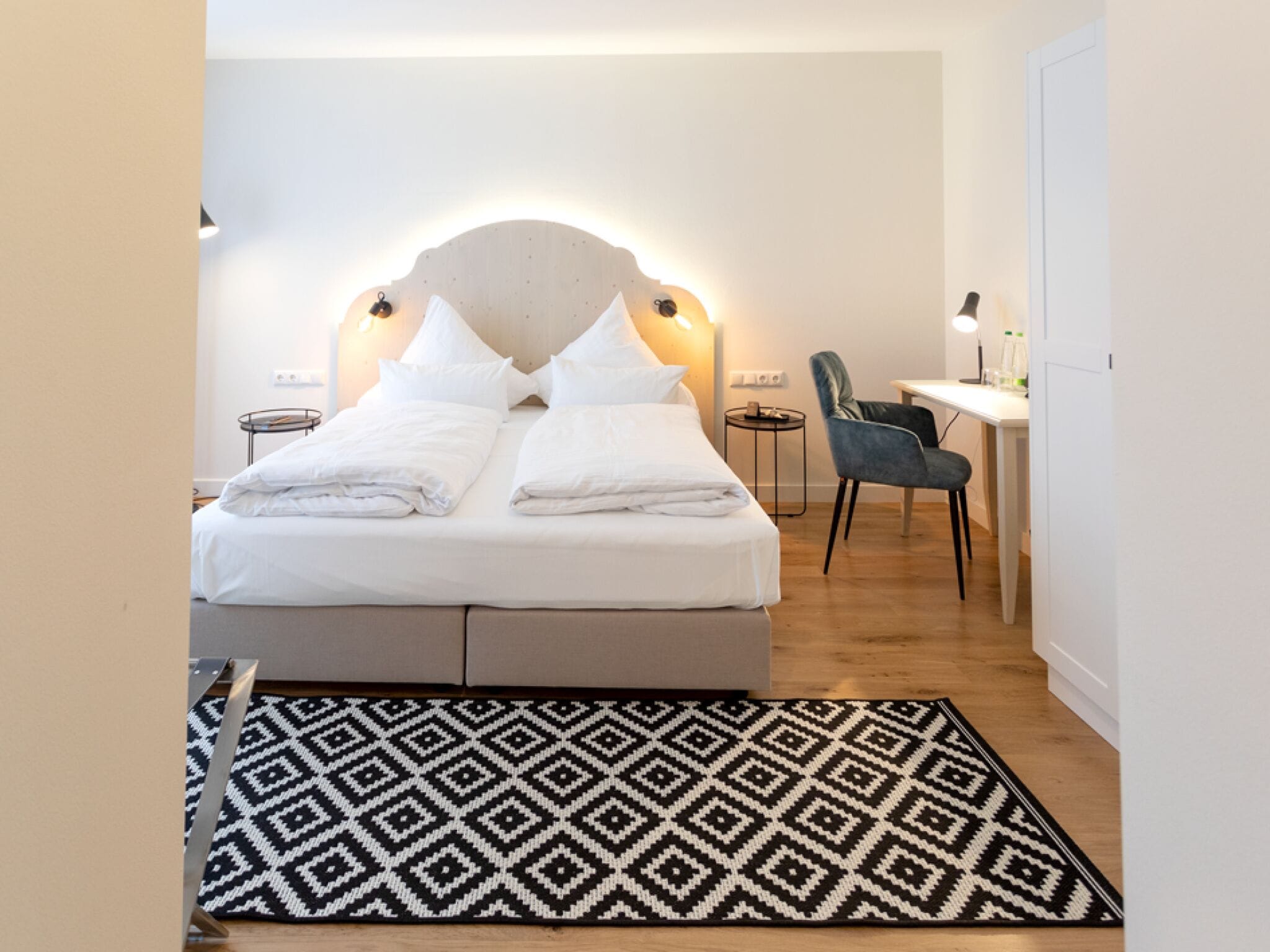 A neatly arranged bedroom with a bed, bedside tables, a desk, and a chair.