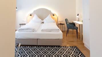 A neatly arranged bedroom with a bed, bedside tables, a desk, and a chair.