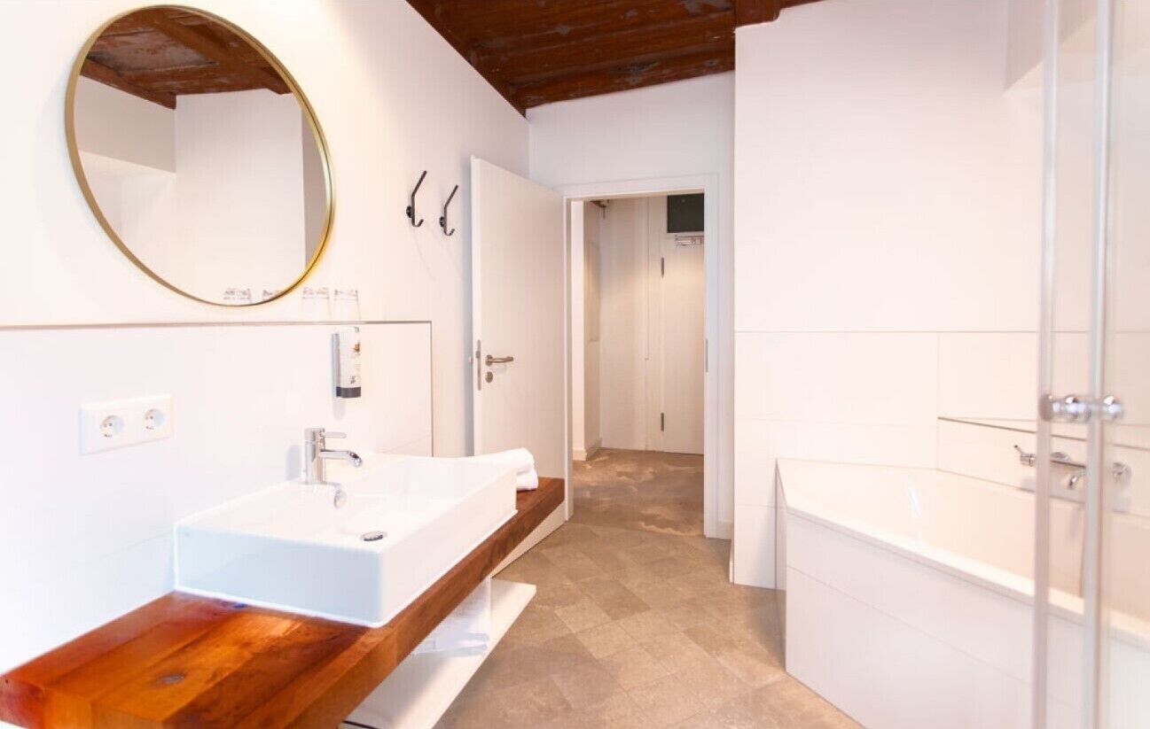 A modern bathroom with a wooden vanity, a large mirror, a white sink, and a bathtub.