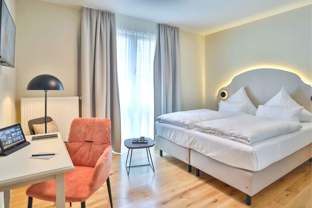 A hotel room with a bed, a desk with a laptop, a chair, and a small table.