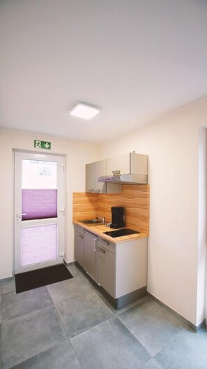 A compact kitchen with a sink, a coffee maker, and a microwave. There is a door with a green emergency exit sign above it. - Landgasthof Scherer (Wenden)