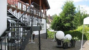 A staircase leading to a balcony with wrought iron railings, a white building with a red roof, and outdoor seating with spherical lamps. - Landgasthof Scherer (Wenden)