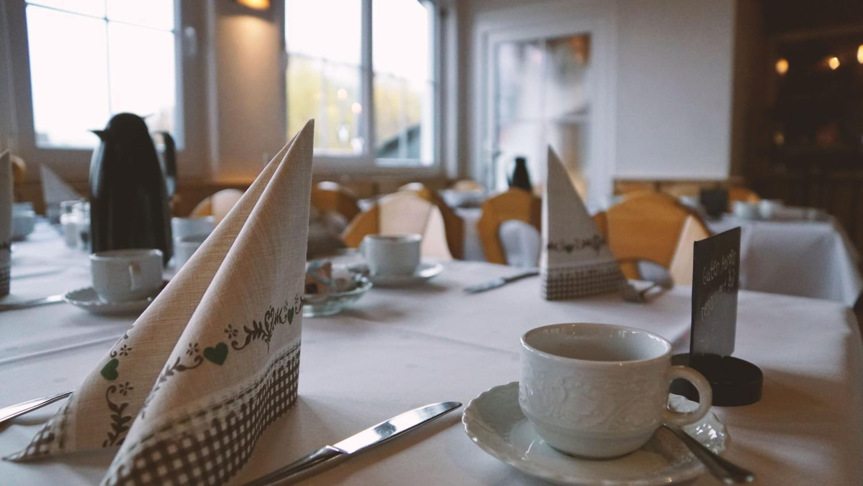 Mesa para comer dispuesta con servilletas blancas, una taza, un platillo y un cuchillo.