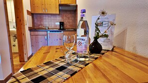 Una mesa de madera con una botella de licor, un vaso y un posavasos en una habitación con armarios de madera y salpicadero de azulejos.