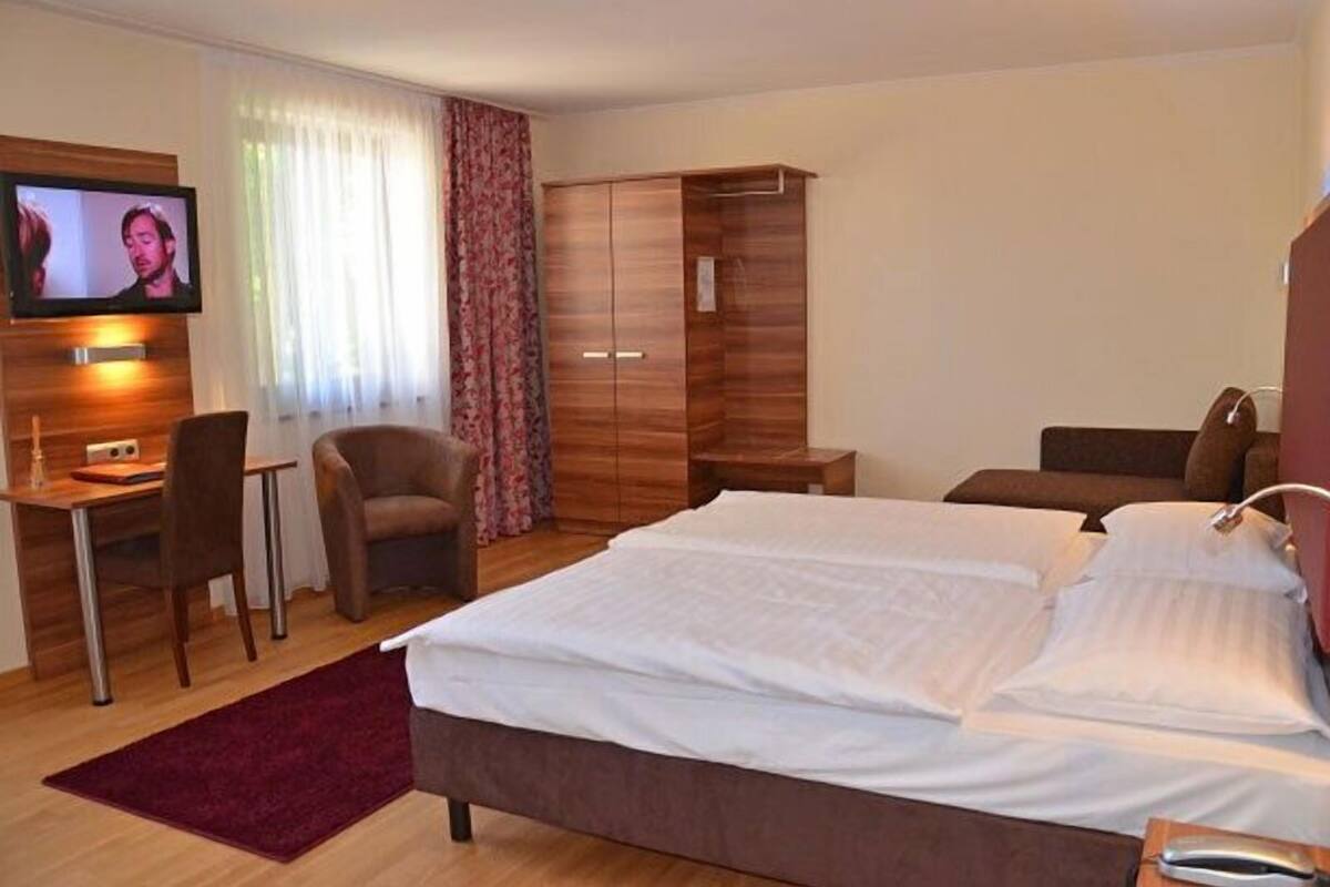 A hotel room with a bed, a desk, a television, a wardrobe, and a chair.
