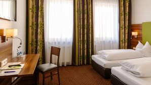 Habitació d'hotel amb escriptori, dos llits, una cadira i un gran finestral amb cortines.