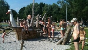 Escena de platja amb una construcció de fusta per jugar i gent participant en diverses activitats.