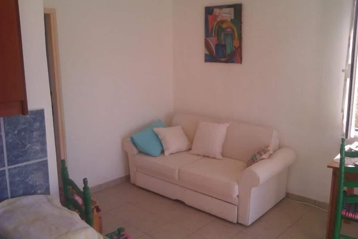 A beige sofa with two pillows, a small painting on the wall, and a wooden chair.