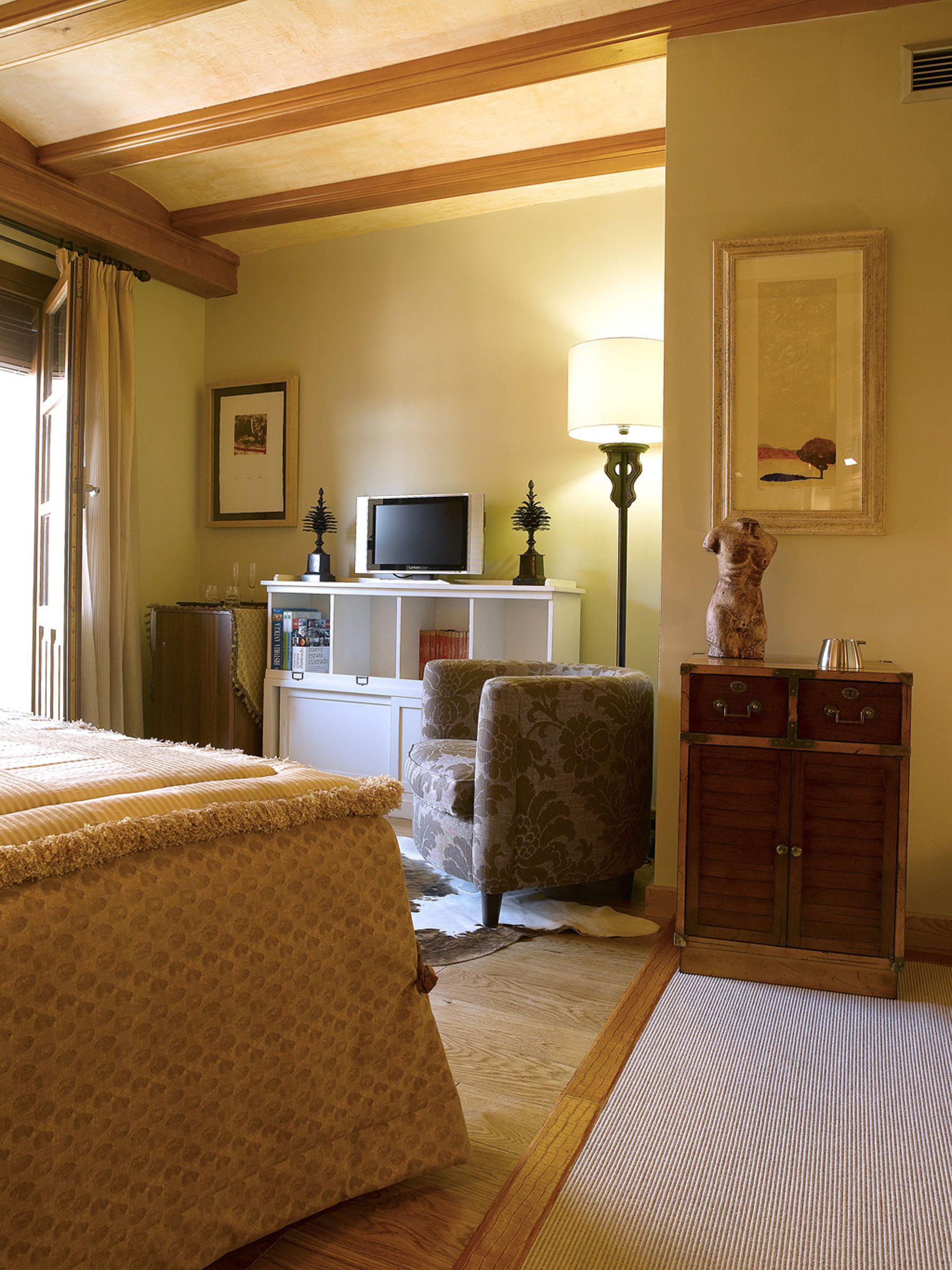 A hotel room with a bed, a chair, a television, a cabinet, and a lamp.