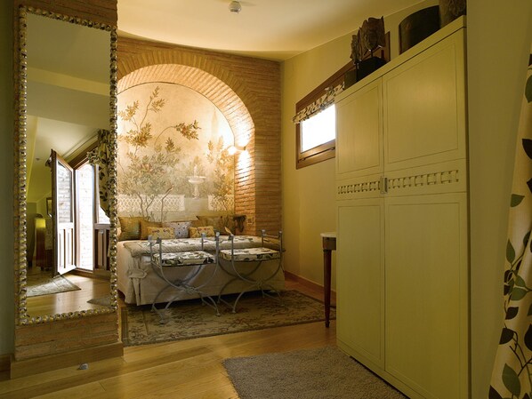 Una habitación con cama, una mesa de comedor y un ventanal arqueado. Hay un espejo en la pared izquierda y un armario a la derecha.