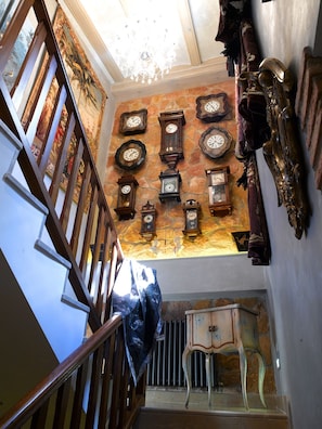 A staircase with a wooden handrail and a wall adorned with multiple antique clocks.